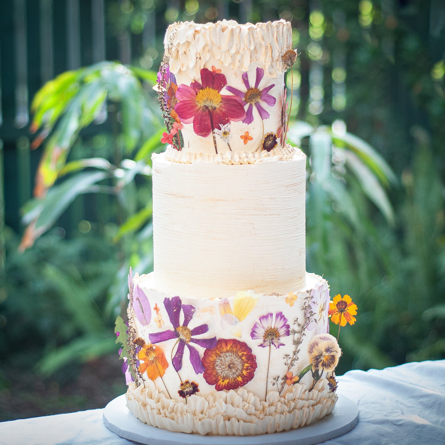 Three-tier buttercream cake decorated with pressed pink and orange flowers, perfect for vibrant wedding celebrations in Brisbane by Caldera.CAKING.