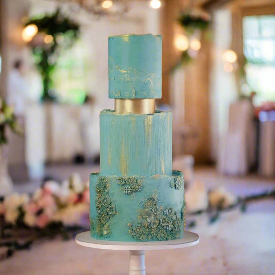 Three-tier wedding cake featuring textured blue buttercream, gold accents, and intricate bas-relief floral detailing, designed for luxury Brisbane weddings by Caldera.CAKING.